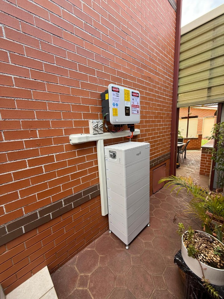 FoxESS battery and inverter on tiled patio against brick wall
